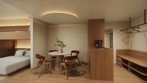 Ein kleines Hotelzimmer mit einem Stockbett, einem runden Esstisch mit Stühlen, einer Kaffeemaschine und einer Bank.