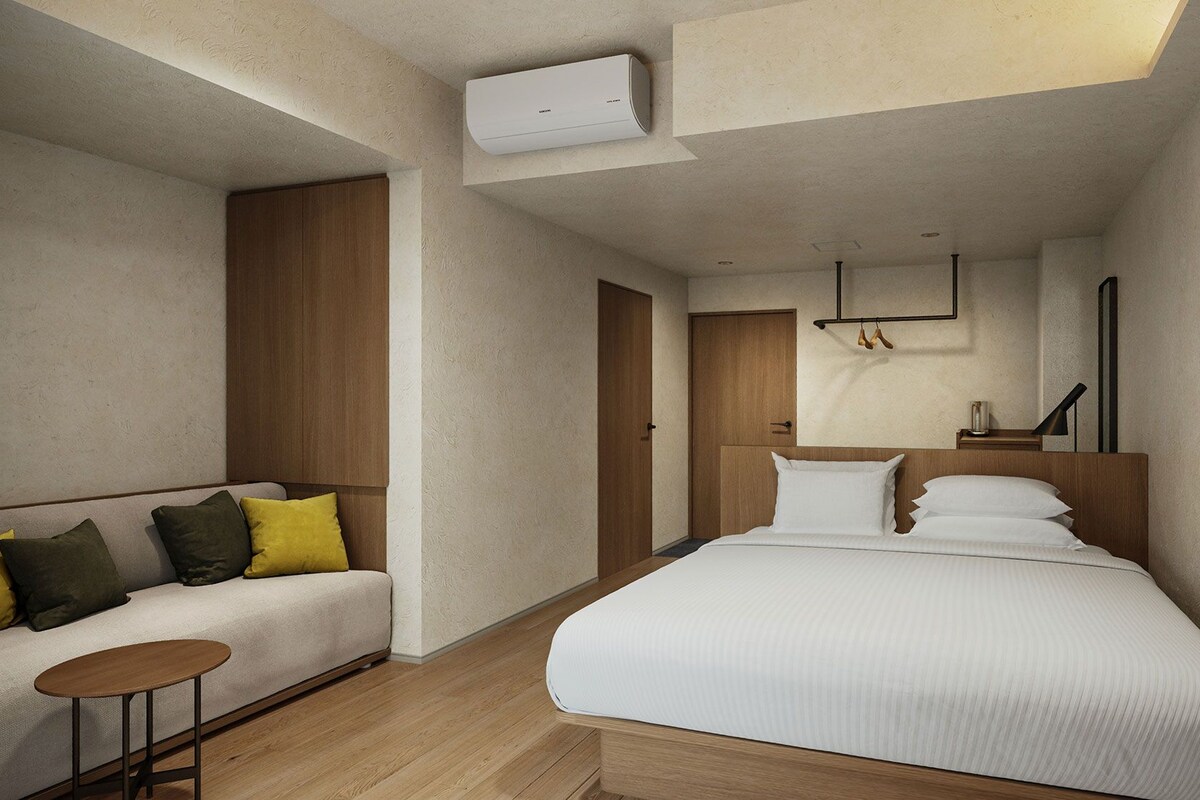 Ein modernes Hotelzimmer mit einem Bett, einer Couch, einem kleinen Tisch und einer Klimaanlage.