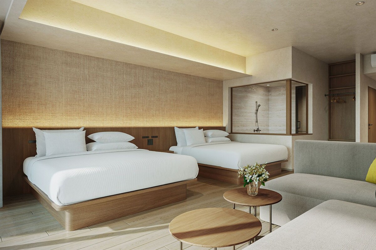 Ein modernes Hotelzimmer mit zwei Betten, einer Sitzecke, einem kleinen Tisch und einer Duschkabine.