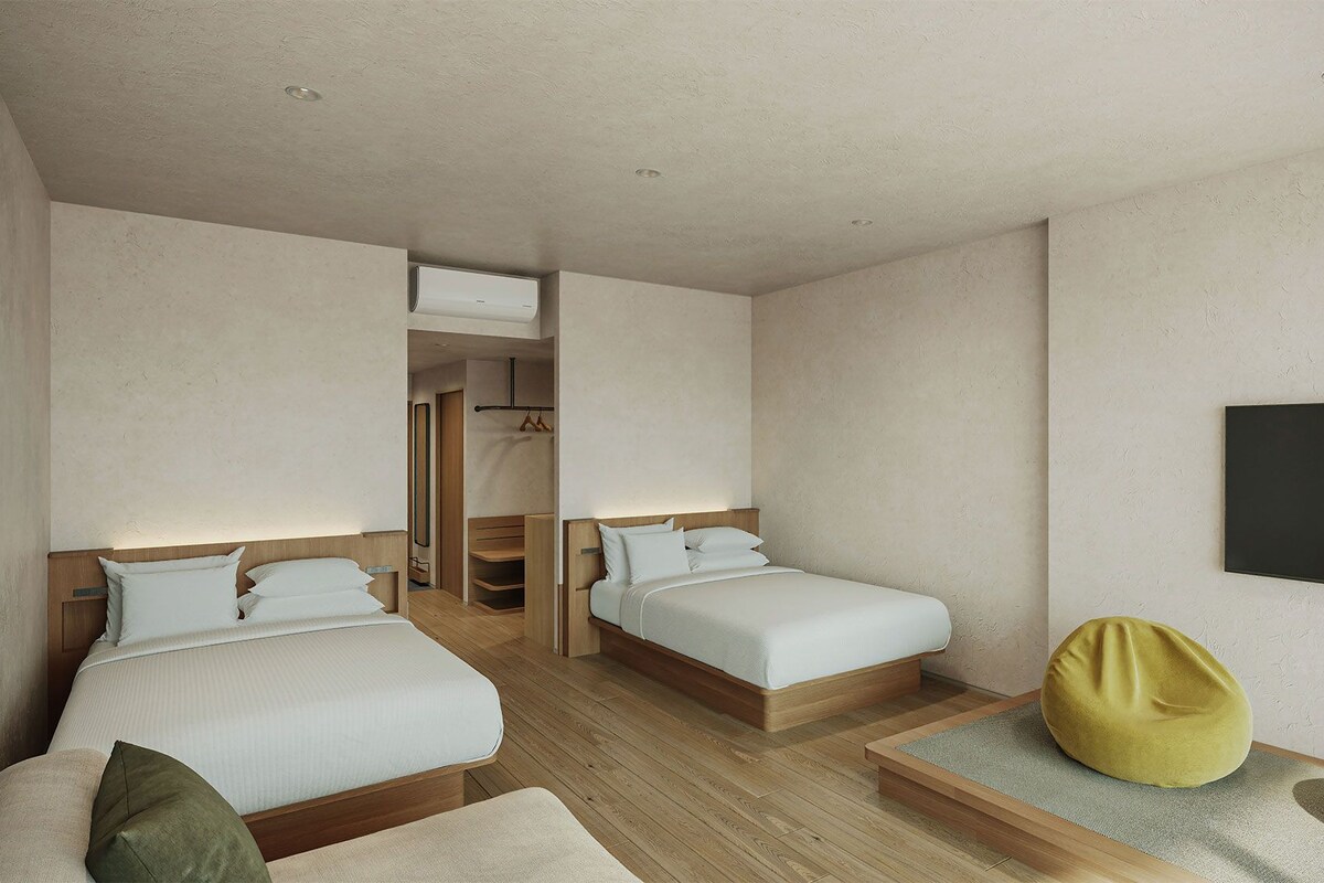 Ein modernes Hotelzimmer mit zwei Betten, einem Kleiderschrank, einem Fernseher und einer Sitzecke.