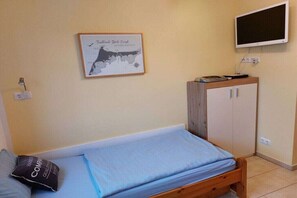 A single bed with a blue mattress and a pillow, a wooden wardrobe, a framed map on the wall, and a television mounted on the wall. - Holiday apartment with 2 bedrooms (Zingst)