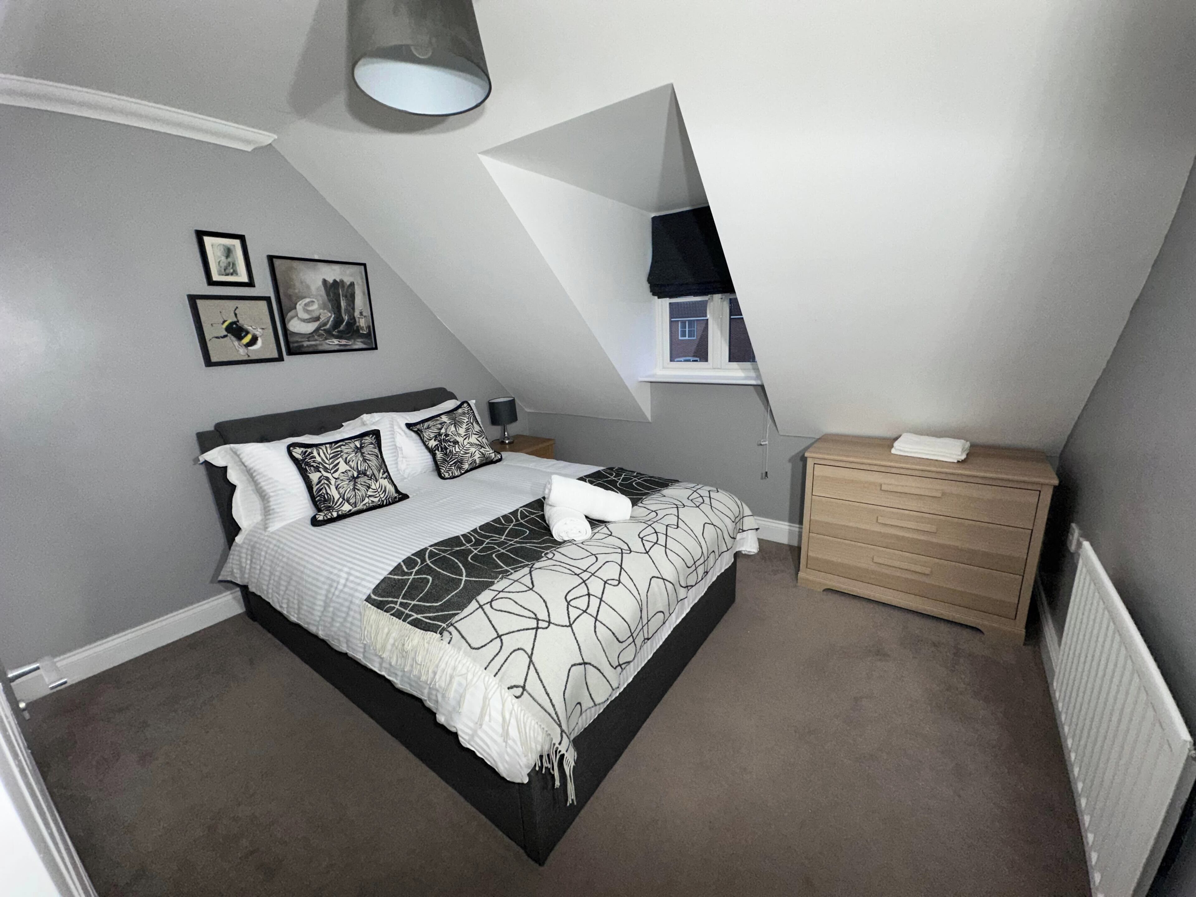 A bedroom with a bed, a nightstand, a dresser, and a window.
