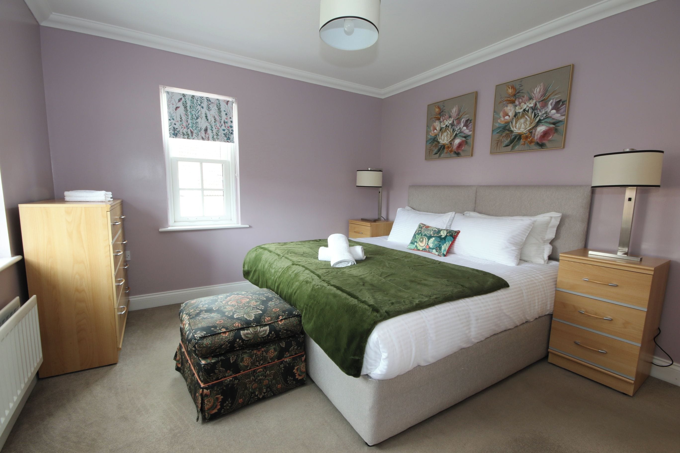 A bedroom with a bed, a nightstand, a dresser, a window, and a radiator.