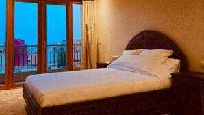 Habitación de hotel con una cama grande, una mesita de noche, una lámpara colgante y vistas de la ciudad a través de amplios ventanales.