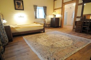 Ein Schlafzimmer mit einem Bett, einem Nachttisch, einer Lampe, einem Sessel, einer Holzkommode und einem großen Teppich.