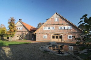 Ein großes, zweistöckiges Gebäude mit einer symmetrischen Fassade, einem zentralen Eingang und einem kleinen Teich im Vordergrund.