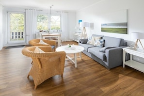 A modern living room with a grey sofa, wicker chairs, a round coffee table, and a painting on the wall. - Holiday apartment in Juist with swimming pool (Juist)
