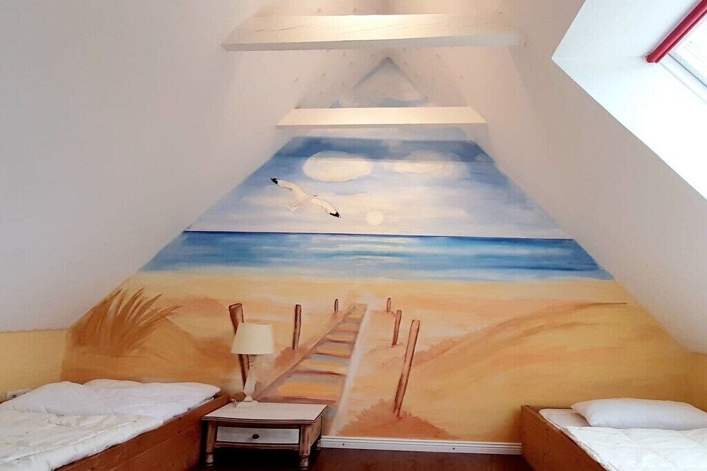 Een kamer met een schuine kap, twee bedden, een nachtkastje en een schilderij van een strand.