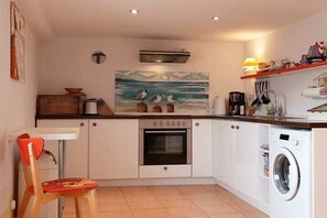A compact kitchen with a washing machine, a stove, and a dining area with a chair. - Holiday apartment with 3 bedrooms (Niesgrau)