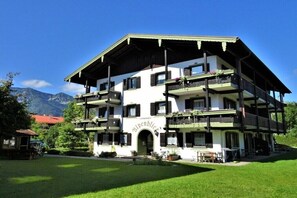 A multi-story hotel with balconies, a central entrance, and a mountainous backdrop. - Holiday apartment with 1 bedroom (Inzell)