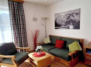 Un salon avec un canapé, des fauteuils, une table basse et un tableau accroché au mur.