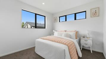 A bedroom with a bed, two bedside tables, a nightstand, and two windows.