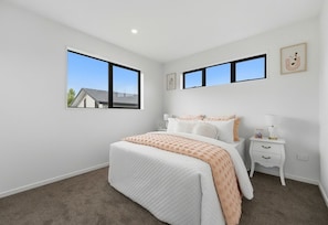 A bedroom with a bed, two bedside tables, a nightstand, and two windows.