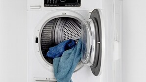 A stacked washer and dryer unit with a blue towel on the top dryer and a blue plastic basin on the bottom dryer.