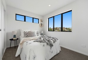 A bedroom with a bed, two bedside tables, a window, and a view of the outside. - Brilliant Howick New Build, Walk to Shops (Auckland)