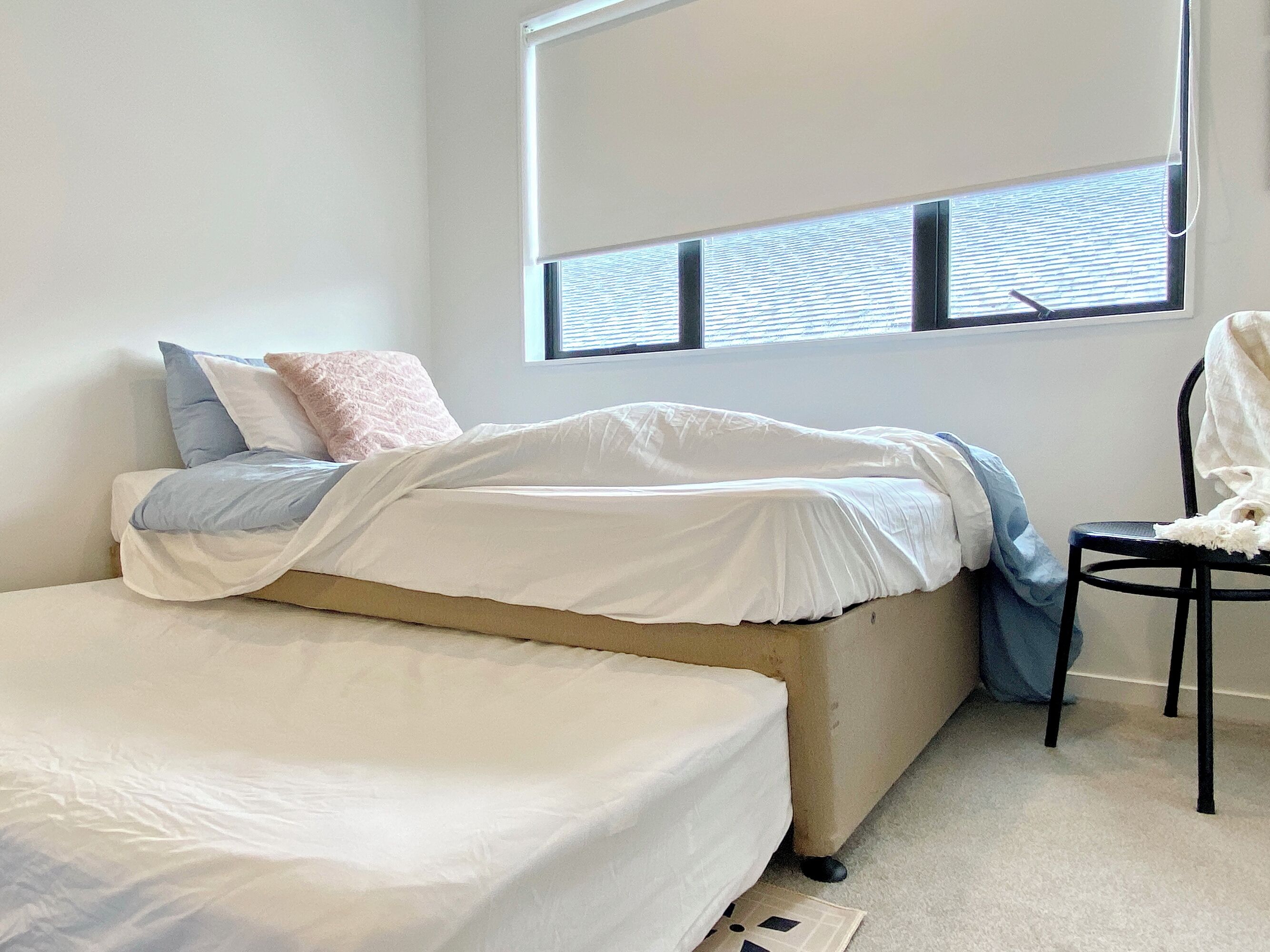 Ein Schlafzimmer mit einem Bett, einem Sessel und einem Fenster mit Jalousien.