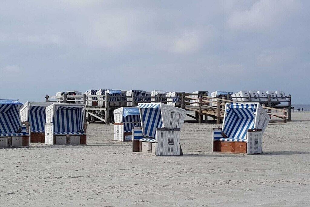 Beach chairs lined up on the sand with a wooden structure in the background.