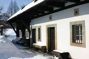 A snow-covered building with a porch, stone steps, and a window with bars. - Holiday home with 1 bedroom (Großschönau)