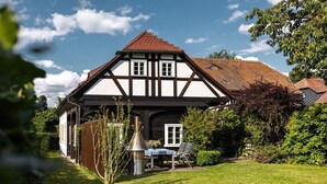 A traditional half-timbered house with a well-maintained garden, a barbecue area, and a clear sky. - Holiday home with 1 bedroom (Großschönau)