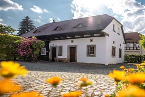 Ein traditionelles weißes Gebäude mit dunklem Dach, einer Kopfsteinpflaster-Auffahrt und einem Garten mit rosa Blumen.