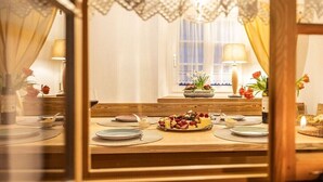 A dining area with a wooden table set for four, a vase of flowers, and a window with curtains. - Holiday home with 1 bedroom (Großschönau)
