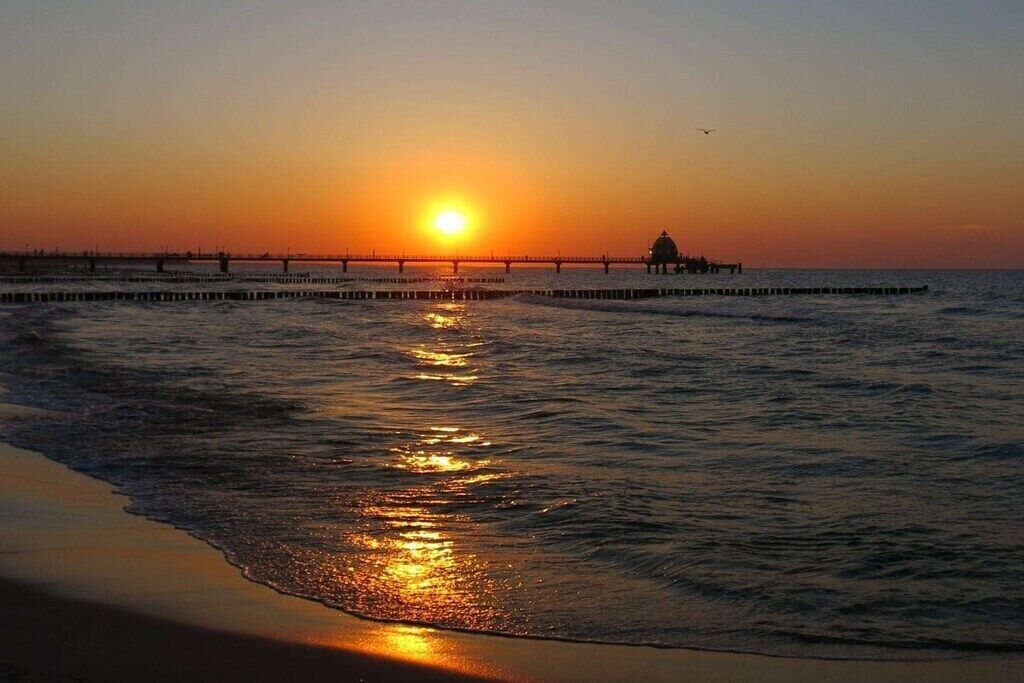 Ein Sonnenuntergang über einem Strand mit einem in das Wasser ragenden Steg.