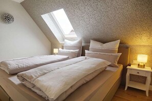 A bedroom with two beds, a skylight, patterned wallpaper, and bedside lamps. - Holiday apartment with 1 bedroom (Zingst)