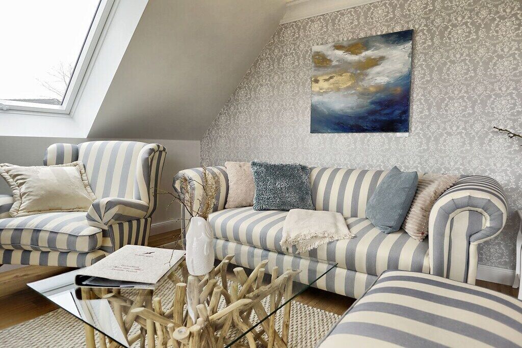 Een woonkamer met een gestreepte bank, fauteuil en een glazen salontafel met decoratie.