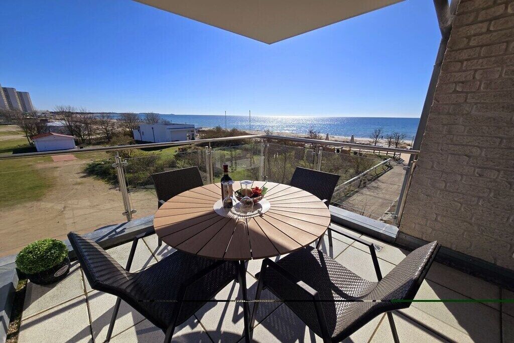 A balcony with a round table and chairs, overlooking a beach and ocean.
