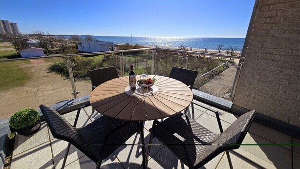 Een balkon met een ronde tafel en stoelen, met uitzicht op een strand en de oceaan.