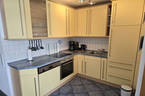 A kitchen with light-colored cabinets, a black stove, a sink, and a coffee maker. - Baltic Sea view south beach Sü 027 (Burg-Tiefe)