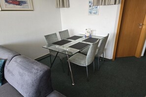 Ein kompakter Raum mit einem Glastisch und vier grauen Stühlen, einem grauen Sofa und einer Holztür.