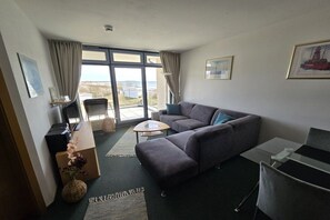 A modern living room with a grey sofa, a small table, and a view through large windows. - Baltic Sea view south beach Sü 027 (Burg-Tiefe)