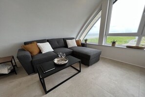 A modern living room with a sectional sofa, a coffee table, and a view of the outdoors through large windows. - Apartment in Huisduinen with swimming pool (Huisduinen)