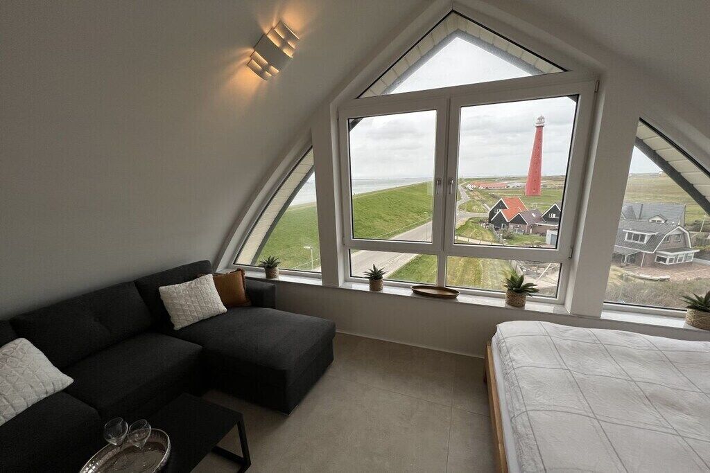Een slaapkamer met een groot raam, een bed, een donkergroene bank en een klein tafeltje met glazen.