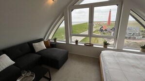 A bedroom with a large window, a bed, a dark-colored sofa, and a small table with glasses. - Apartment in Huisduinen with swimming pool (Huisduinen)