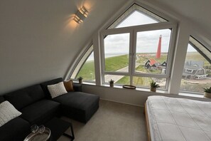 Een slaapkamer met een groot raam, een bed, een donkergroene bank en een klein tafeltje met glazen.