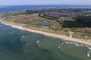 Luchtbeeld van een kustgebied met een strand, een stad op de achtergrond en een groot waterlichaam.