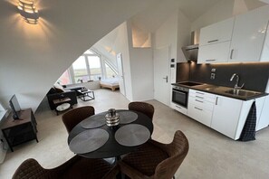 Een moderne keuken met witte kasten, een zwart aanrecht en een eethoek met een ronde tafel en bruine stoelen.