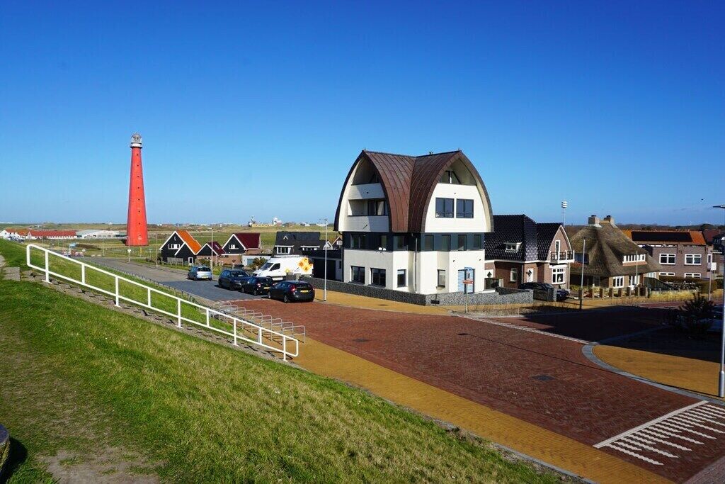 Een gebouw aan de kust, met een opvallend rode vuurtoren op de achtergrond.