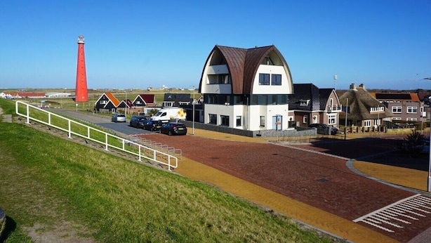 A coastal building with a prominent red lighthouse in the background. - Apartment in Huisduinen with swimming pool (Huisduinen)