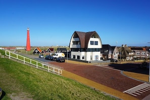 A coastal building with a prominent red lighthouse in the background. - Apartment in Huisduinen with swimming pool (Huisduinen)