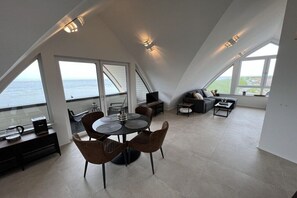 Een ruime loft met een eetgedeelte, zitplaatsen en grote ramen met uitzicht op de oceaan.
