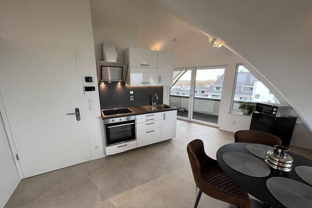 A modern kitchen with a built-in oven, microwave, and a dining area with a table and chairs.