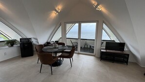 A dining area with a table and chairs, a television, and a view of the sea through large windows. - Apartment in Huisduinen with swimming pool (Huisduinen)