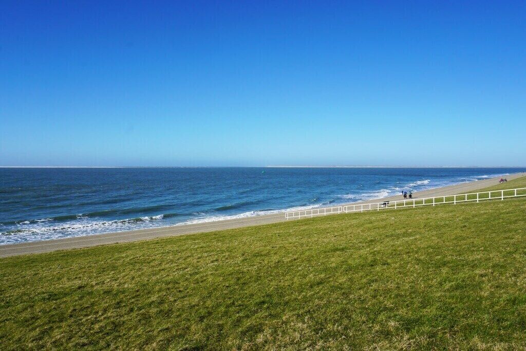 Een kustlandschap met een grasveld en een strand met een witte omheining.