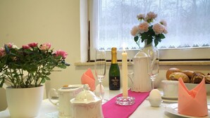 Ein Tisch ist gedeckt mit einer Weinflasche, Gläsern, einer Kerze, einer Blumenvase und einer Auswahl an Gebäck.
