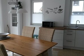 Uma cozinha com mesa de madeira, cadeiras de vime, micro-ondas e um adesivo de parede.