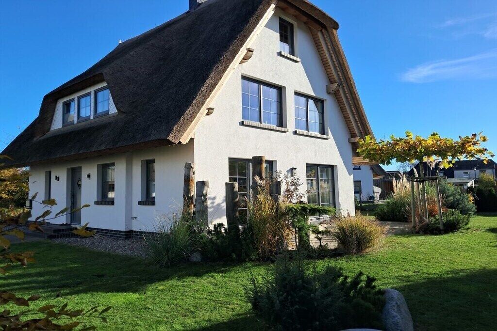 Une maison à deux étages, avec un toit de chaume, des murs extérieurs blancs et de nombreuses fenêtres.