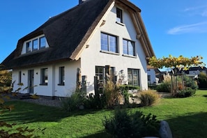 Ein zweistöckiges Haus mit Strohdach, weißen Außenwänden und zahlreichen Fenstern.